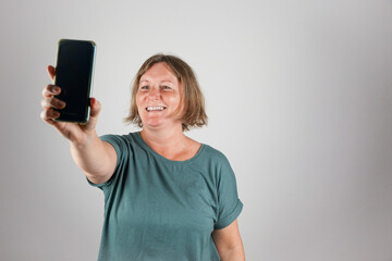 Naklejka premium Eine Frau über 50 macht ein Selfie mit einem Smartphone. Studio, neutraler Hintergrund.
