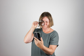Eine Frau über 50 schaut  durch eine Lupe auf ein Smartphone. Sehschwäche, Humor.