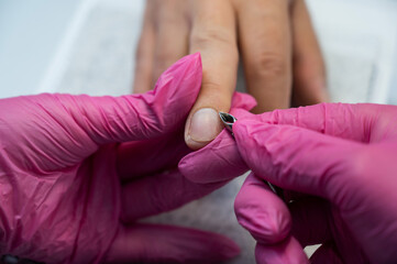 Manicurist cuts off cuticle to male client using nippers. 