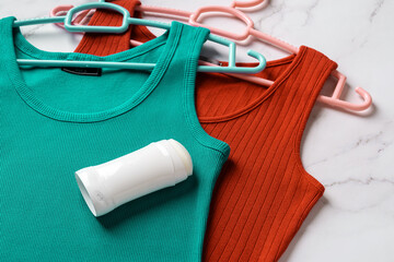 Solid deodorant on teal and red tank tops over marble background. Antiperspirant stick on a linen jersey tank shirts on hangers. Body care, skin care, toiletries and hygiene concept.