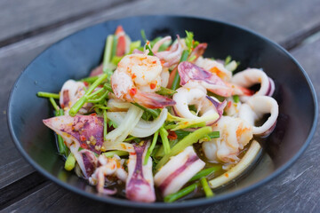 Spicy salad with shrimp and squid was mixed with chopped tomato and onion on the black dish.