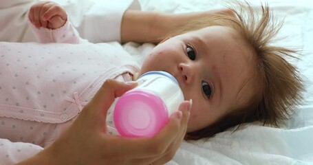 Unknown loving mother holding bottle feeds her newborn daughter, 0-6 baby girl drinks moms breast milk resting lying on bed. Balanced artificial feeding of infant formula, nutrition, babyhood concept