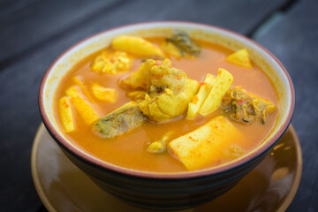 Spicy sour yellow curry with  coconut shoots and sea fish is one of Southern of Thai food on wood table as a background.