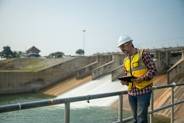 Fototapeta na wymiar Portrait of engineer wearing yellow vest and white helmet with tablet Working day on a water dam with a hydroelectric power plant. Renewable energy systems, Sustainable energy concept