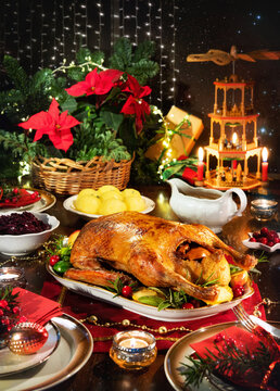 Roast duck served on a festive family table prepared for Christmas dinner. Decorations with candles, lights, Chrismas pyramid and gifts
