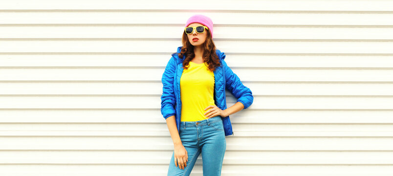 Portrait of stylish young woman model wearing colorful pink hat, blue jacket on white background