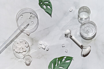 Home made moisturizer and white stone face rollers, pipette on off white marble background. Beauty treatment background, lat lay. Handmade cosmetics background with monstera. Direct sunlight, shadows.