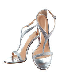 Pair of elegant women's open silvery color leather strappy sandals tied with a bow, with a high thin heel, isolated on a white background. The bride's shoes for the wedding ceremony.