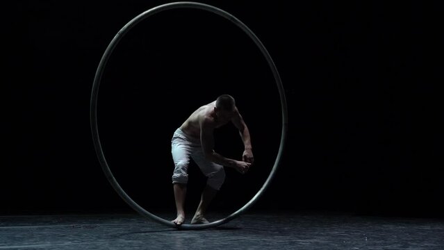 Muscular circus artist perform Cyr Wheel on a black background. Concept of willpower, motivation and passion