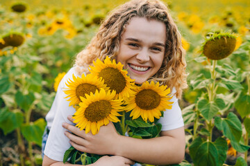 Smiling beautiful curly woman rejoices and enjoying sunflower field on a sunny day. Natural beauty. Nature landscape. Smiling girl