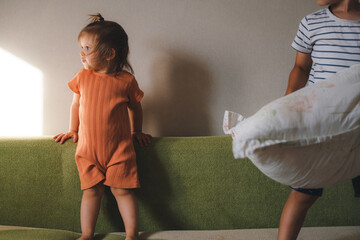Baby girl standing on the sofa looking away, she doesn't want to continue the pillow fight with her...