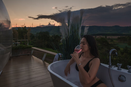 Back View Woman Pampering Her Body In Water While Lie In Bath Tube Outdoor With Jungle And Mountains View Eat Wine On Vacation Travel