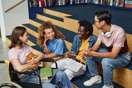 Diverse Group Of Young People Discussing Work In College Library Including Female Student With Disability