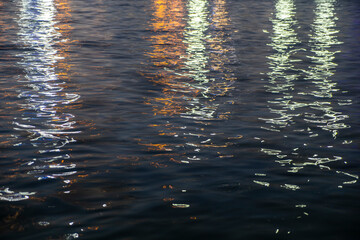 Reflection of colorful lights on the sea surface at night, water waves at night, background, texture, abstract. Selective focus, noise effect and grainy texture. 