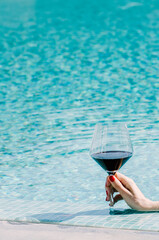 Female hand holding glass of red wine, on turquoise water background. Travel vacation. Luxury cruise. Summer holidays. Female manicure. Luxury resort hotel vacation