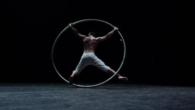 Muscular circus artist perform Cyr Wheel on a black background. Concept of Individuality and creativity 