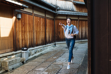 full length excited asian female tourist is shouting and pointing into distance while running...