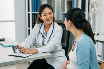 Fototapeta premium asian female gynecologist is smiling while showing and explaining an ultrasound picture to her expectant patient at the office desk in the clinic.
