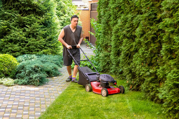 middle aged handsome man wearing home clothes is cutting the lawn, process to cut the grass at the yard with special machine lawn mover, green garden