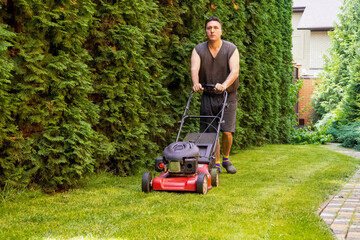 middle aged handsome man wearing home clothes is cutting the lawn, process to cut the grass at the yard with special machine lawn mover, green garden