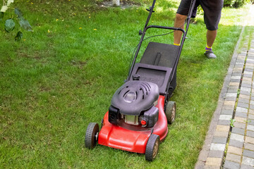 middle aged handsome man wearing home clothes is cutting the lawn, process to cut the grass at the yard with special machine lawn mover, green garden