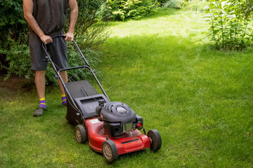 middle aged handsome man wearing home clothes is cutting the lawn, process to cut the grass at the yard with special machine lawn mover, green garden