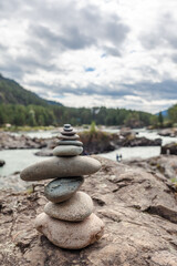 Fototapeta na wymiar A pyramid of bare stones stacked on top of each other. Stones stacked in the shape of a pyramid on the riverbank against the background of mountains as balance and balance in nature, Zen, Buddhism.