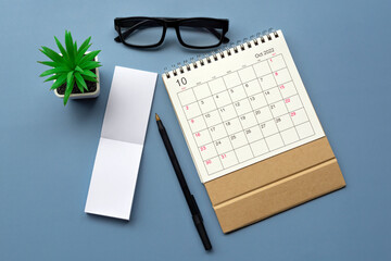 October 2022 desk calendar with notepad on blue background. Copy space.
