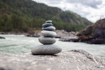A pyramid of bare stones stacked on top of each other. Stones stacked in the shape of a pyramid on the riverbank against the background of mountains as balance and balance in nature, Zen, Buddhism.