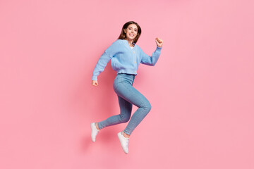 Fototapeta na wymiar Profile side full length photo of satisfied beautiful cute nice girl dressed blue knit pullover jumping run in air clench fists isolated on pink color background