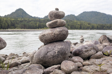 A pyramid of bare stones stacked on top of each other. Stones stacked in the shape of a pyramid on the riverbank against the background of mountains as balance and balance in nature, Zen, Buddhism.