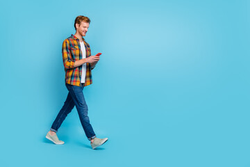 Full size photo of handsome stylish guy red hairstyle dressed checkered shirt look in smartphone walk isolated on blue color background