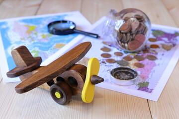 On a wooden desk a retro model of airplane on the background of maps, compass, magnifier and glass jar of coins. The concepts of transport, travel, business.
