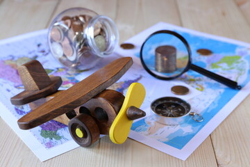 On a wooden desk a retro model of airplane on the background of maps, compass, magnifier and glass jar of coins. The concepts of transport, travel, business.