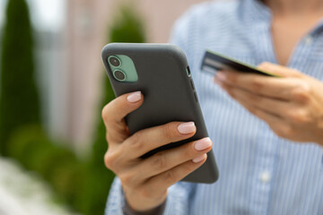 female hands hold a modern mobile phone and a bank credit or debit card on the street..ordering purchases, working online, transferring money by phone