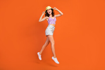 Full length photo of pretty excited lady purple swimwear jumping high walking empty space isolated orange color background