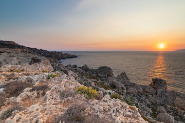 Fototapeta na wymiar A colourful sunset over the cliffs of Paradis bay in Malta with a view on the Island of Gozo in the Mediterranean Sea. In summer the countries around the Mediterranean enjoy every evening these sunset