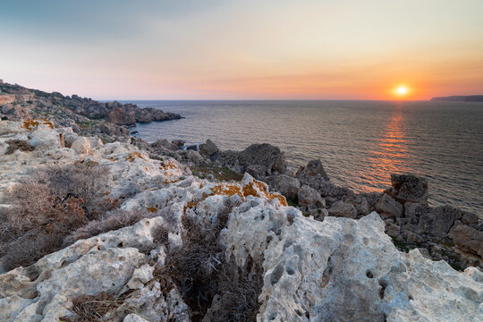 A colourful sunset over the cliffs of Paradis bay in Malta with a view on the Island of Gozo in the Mediterranean Sea. In summer the countries around the Mediterranean enjoy every evening these sunset