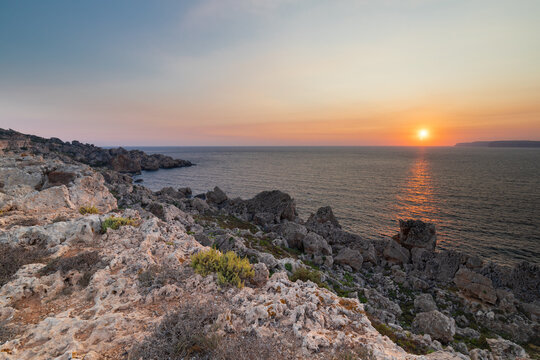 A colourful sunset over the cliffs of Paradis bay in Malta with a view on the Island of Gozo in the Mediterranean Sea. In summer the countries around the Mediterranean enjoy every evening these sunset