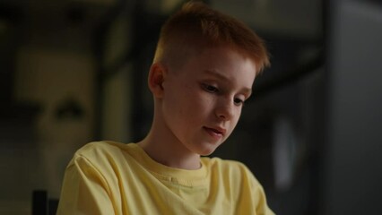 Close-up face of thoughtful schoolboy typing on laptop computer and thinking with hands on chin. Pupil boy learning lesson at school, making homework and using notebook gadget. Shooting in slow motion