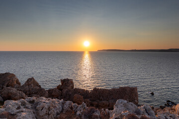 Obraz premium A colourful sunset over the cliffs of Paradis bay in Malta with a view on the Island of Gozo in the Mediterranean Sea. In summer the countries around the Mediterranean enjoy every evening these sunset