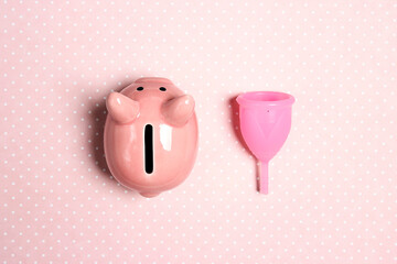 Menstrual cup with piggy bank on a pink polka dot background.