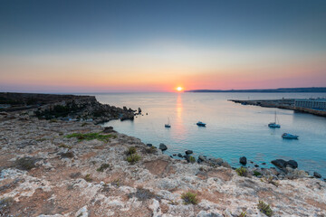 A colourful sunset over the cliffs of Paradis bay in Malta with a view on the Island of Gozo in the Mediterranean Sea. In summer the countries around the Mediterranean enjoy every evening these sunset