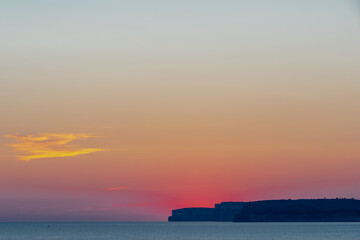 A colourful sunset over the cliffs of Paradis bay in Malta with a view on the Island of Gozo in the Mediterranean Sea. In summer the countries around the Mediterranean enjoy every evening these sunset