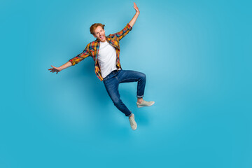 Fototapeta na wymiar Photo of cheerful positive guy with ginger hair dressed checkered shirt jumping flying open mouth isolated on blue color background
