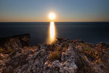 Amazing sunrise over the rising cliffs and rocks at Mellieha in the north west of Malta, with spectacular colors in the sky and reflections of the sun in het Mediterranean sea