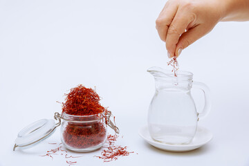 A glass jar filled with saffron stamens and a woman putting red stamens into water in a decanter on...