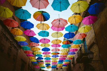 Fototapeta na wymiar Colorful umbrellas hanging above city street.. Colorful umbrellas hanging in the sky used as street decoration.