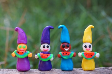 Figures of colorful dwarfs hold watermelons in their hands and smile. Positive mood. The emotion of joy.