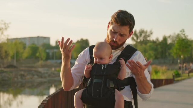 Close up attractive young father holding a child talking show something funny newborn baby not reacting sitting in a slings carrier. Ergo backpack. Parents. Slow motion